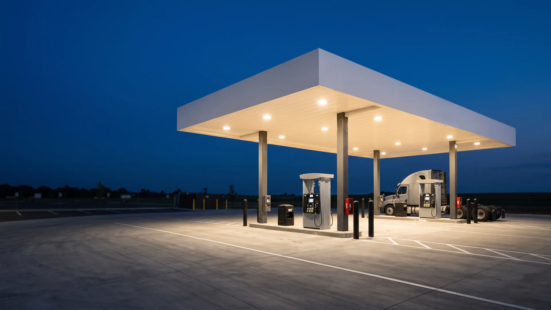 Fleet fueling canopy glowing at dusk over two concrete fueling islands with a semi tractor parked