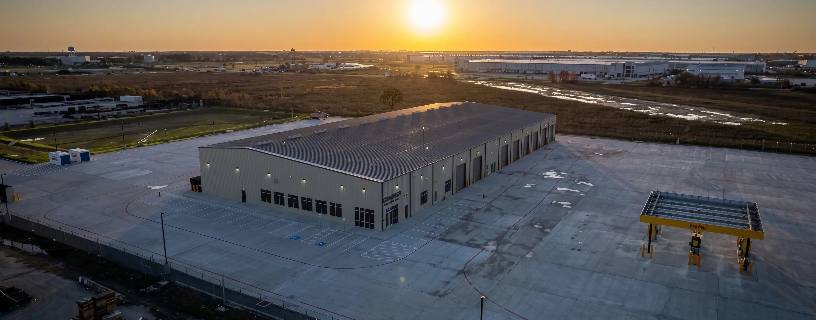 Aerial view of the Penske Katy Service Center at sunset with its truck bays, paved yard, and the industrial corridor beyond